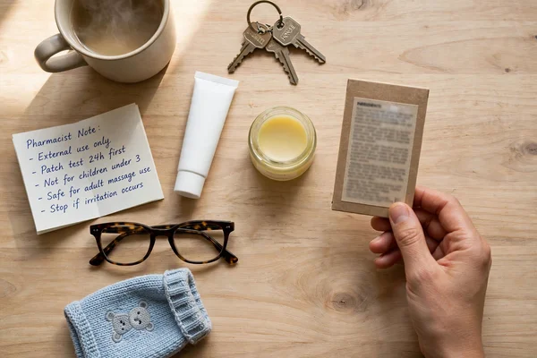 Bálsamo labial sin marca sobre mesa de madera, gafas, nota del farmacéutico y paquete de ingredientes.