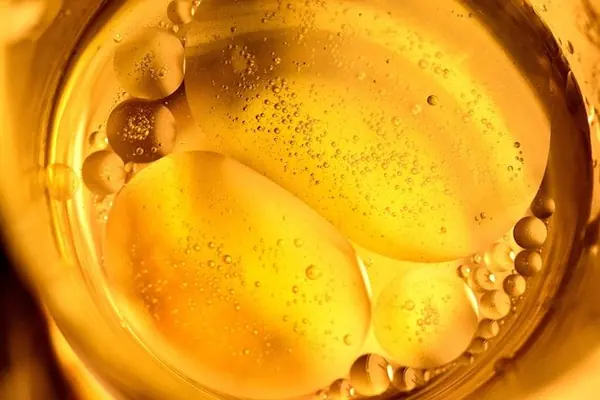 Mujer de unos 40 años sentada en una mesa de cocina, mirando pensativamente un pequeño frasco de suplemento opaco sin marca. A su lado, un cuaderno abierto y un vaso de agua a medio llenar.