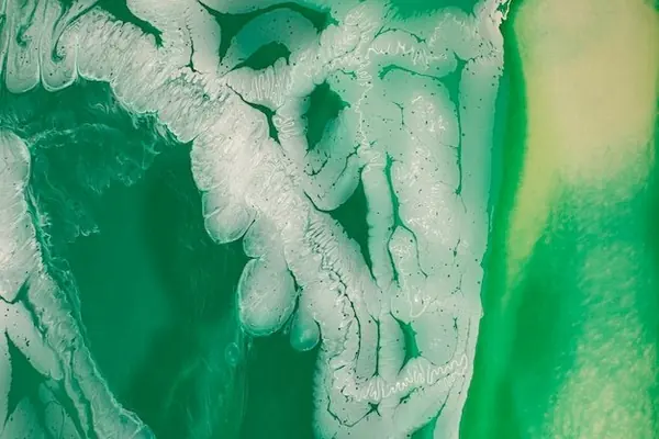 Primer plano de una mujer de unos 40 años, iluminada lateralmente, sentada cerca de una ventana y mirando una botella de plástico genérica sin marca que sostiene en la mano.
