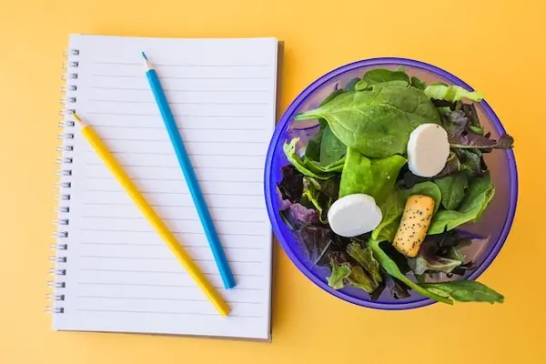 Persona leyendo una etiqueta de nutrición en un entorno de oficina en casa, con luz de ventana y una planta pequeña en el escritorio.