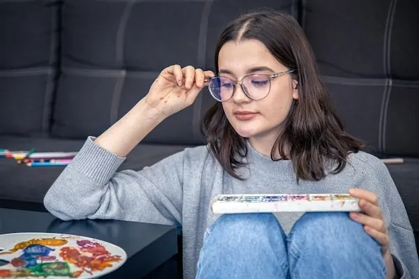 Persona de mediana edad limpiando sus gafas con un paño en una mesa de madera en un interior soleado.
