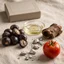Bodegón editorial con ingredientes de Adenofrin: bayas de palma enana americana, corteza de ciruelo africano, tomate, aceite y formas minerales.