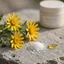 Bodegón fotorealista con flores de árnica, cristales de mentol y una gota de aceite de vitamina E sobre superficie de piedra.