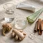 Bodegón editorial con ingredientes naturales del producto Priapus: agua, propilenglicol, raíz de maca, jengibre, canela, aloe vera y ácido hialurónico.